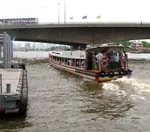 Chao Phraya river bus crowded with passengers passing under a Bangkok bridge