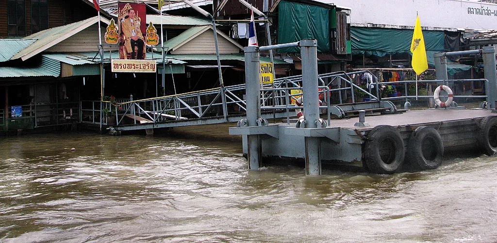 Riverside Chao Phraya River dock with wooden stalls, high water and ferry passengers